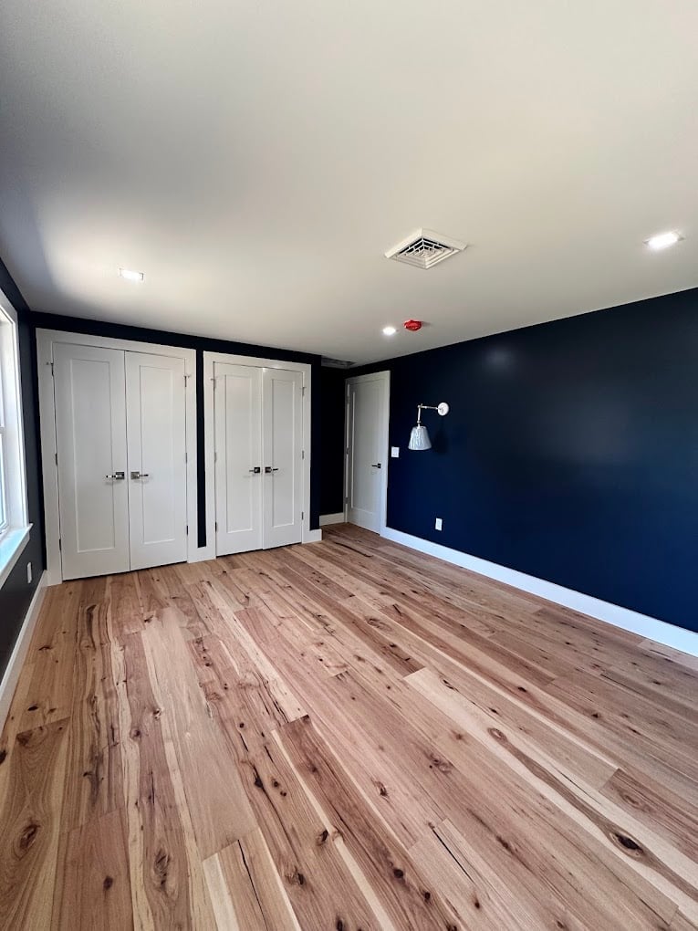 Empty bedroom with dark blue walls, white double doors, wood flooring, and recessed ceiling lights