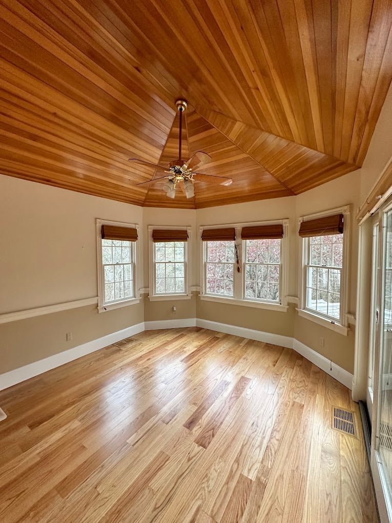 Sunroom with vaulted wooden ceiling, hardwood floors, multiple windows with white trim, cream walls, and ceiling fan