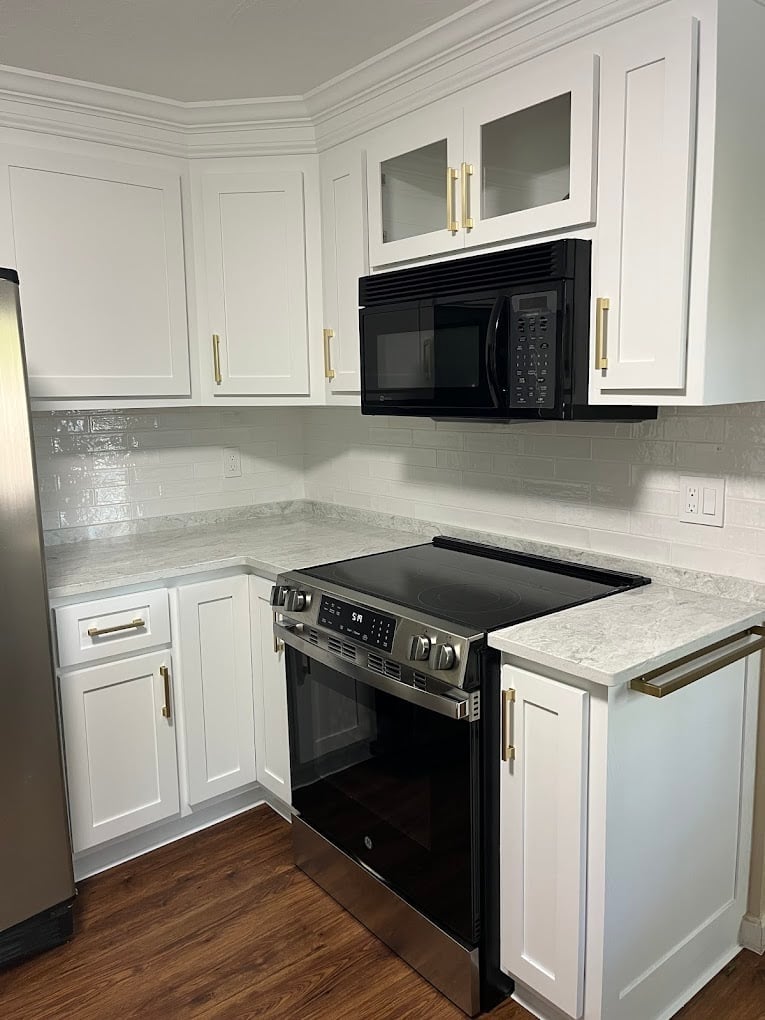Modern kitchen corner with white cabinets, stainless steel black range, white marble countertops, subway tile backsplash, and wood flooring